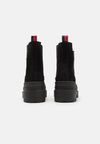 Botine negre din suede cu o talpă groasă, cusături verticale laterale și un tab de prindere multicolor în spate.