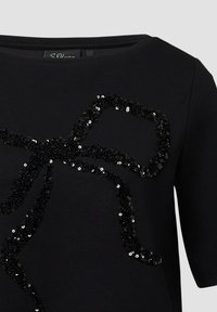 Črni kratkosrajčni top z bleščečim dizajnom, podoben loku, v črni barvi. Mehka tkanina z gladko teksturo in okroglo ovratnikom.