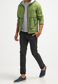 Light green zippered jacket with hood, gray T-shirt underneath, black pants, and navy slip-on shoes. Textured fabric with black accents.