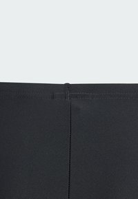 Leggings neri a vita alta caratterizzati da un tessuto liscio ed elastico, con una cucitura che scende lungo la schiena e un design minimalista.