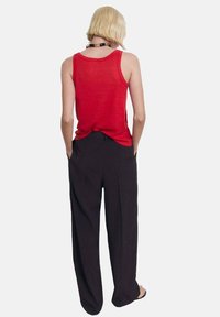 Red sleeveless top with a relaxed fit, paired with black wide-leg trousers. Smooth texture and simple design, featuring a classic neckline.