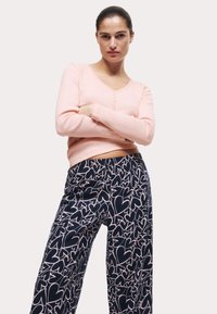 Helles rosa Langarmshirt mit V-Ausschnitt und Knöpfen, kombiniert mit dunkelblauen Hosen mit einem weißen Herzmuster. Weicher Stoff, lässige Passform.