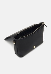 Svart läder clutchväska med en slät textur, guldfärgad dragkedja och beslag, samt en cirkulär magnetskapsel. Öppen för att visa insidan.