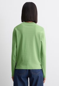 Groene longsleeve t-shirt van zacht katoen, met een ronde hals en een losse pasvorm, gecombineerd met donkerblauwe denim jeans.