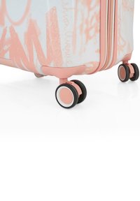 Maleta rígida con una superficie texturizada en blanco y rosa, con acentos en rosa, doble cierre y cuatro ruedas negras con bordes blancos.