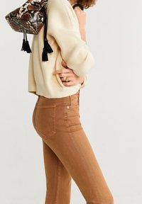 Pull en tricot crème, jean taille haute marron. Sac à motif serpent avec des franges noires. Palette de couleurs chaudes, coupe décontractée.