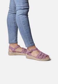 Pink suede sandals with strappy design, open toe, and ankle strap. Featuring a woven espadrille sole. Paired with light blue jeans.