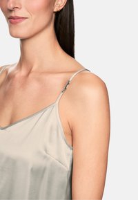 Satin camisole in soft beige with thin straps, featuring a subtle triangular cut and a small pocket detail on the side.
