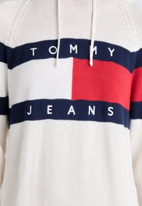 Felpa bianca a maglia con strisce orizzontali blu navy e rosse. "TOMMY" e "JEANS" sono in mostra in bianco sulla striscia blu navy.