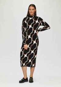Langsl sleeve jurk in zwart en wit met een abstract patroon en bruine accenten. Heeft een hoge hals en een rechte silhoët, gemaakt van een gladde stof.