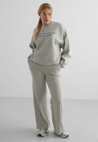 Gray sweatshirt and matching pants in soft fabric, featuring a graphic text design on the front. Loose fit with a comfortable style.