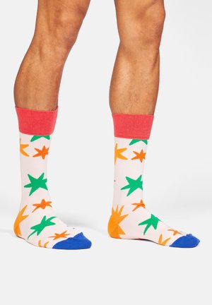 Mehrfarbige Socken mit einem pinken Bündchen, die grüne und orangefarbene Sternmuster auf weißem Hintergrund und blaue Zehenakzente aufweisen.