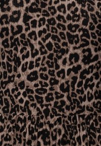 Hladká látka s leopardím vzorem v béžové a černé barvě, s texturovaným povrchem a různými tvary vzoru, s jemným skládáním na spodní části.