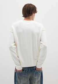 Witte gebreide trui met geribbelde manchetten en rand, met een ontspannen pasvorm en subtiele textuur, gecombineerd met blauwe denim jeans met oversized zakken.