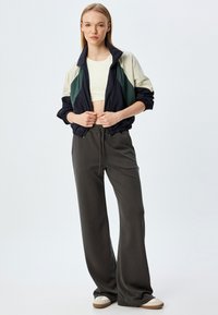 Sportieve jas in navy, crème en groen, gecombineerd met grijze high-waisted broek. Gladde stof, relaxte pasvorm, met een trekkoord in de taille.