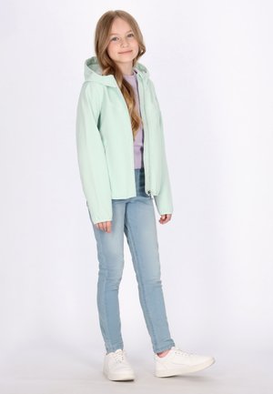Helle mintgrüne Jacke mit Kapuze, Reißverschluss vorn und kontrastierender Innenauskleidung, kombiniert mit hellblauen Jeans und weißen Sneakers.
