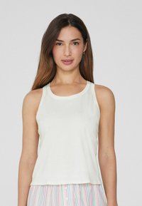 Top de tirantes de crema clara con escote redondo y tirantes anchos. Fabricado con un tejido suave y un ajuste relajado, ligeramente holgado.