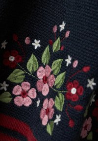 Marinblå stickad tyg med broderade blomsterdesigns i rött, rosa och vitt, med gröna blad och ytterligare accenter.