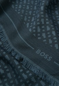 Dark blue scarf featuring a textured pattern, fringed edges, and a subtle logo. Material appears soft with a woven design.