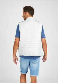 Lichte, gewatteerde mouwloze vest in het wit, met een staande kraag en zwarte accenten, gecombineerd met een blauwe T-shirt met korte mouwen en denim shorts.