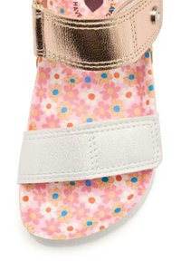 Correas metálicas en oro rosa y plata sobre una plantilla de color rosa con un patrón floral, que presenta pequeñas flores azules y naranjas y un acabado texturizado.