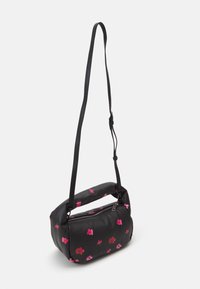 Sac à bandoulière noir avec motif de fleurs roses, poignée rembourrée et longue sangle réglable, présenté suspendu sur un fond blanc.