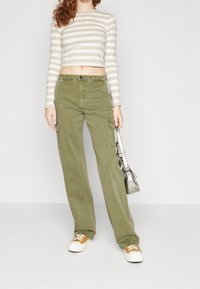 Long-sleeve, cropped top with beige and white stripes; olive green cargo pants with side pockets; white sneakers with orange accents; silver handbag.