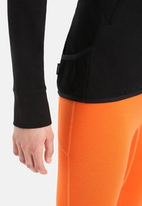 Maglia nera a maniche lunghe con tessuto strutturato e foro per il pollice, abbinata a leggings arancioni vivaci con cuciture piatte e vestibilità aderente.