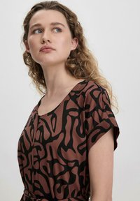 Kurzärmeliges Kleid in Braun-Schwarz-Muster mit Rundhalsausschnitt und lockerer Passform, das ein abstraktes Design und eine weiche Stofftextur aufweist.
