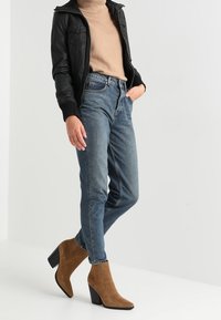 Svart läderjacka, beige tröja, blå denimjeans och bruna ankelboots med en kraftig svart klack. Avslappnad outfit med en figurnära look.
