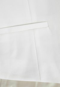 Biała tkanina o gładkiej strukturze, z ukośnym szwem i wąskim złożonym detalem, tworząca uporządkowany design.