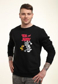 Svart sweatshirt med en illustration av tecknade figurer Tom och Jerry. Rund hals, långa ärmar, med en texturerad bomullsfinish.