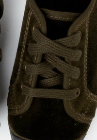 Olivově zelené tenisky s texturovanou tkaninou, kulatou špičkou a plochými tkaničkami. Mají hnědé prošívání a gumovou podrážku s jemným vzorem.