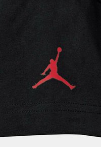Tessuto nero con un'iconica silhouette rossa del logo Air Jordan, che rappresenta una figura in volo con un pallone da basket. Design semplice e texture.