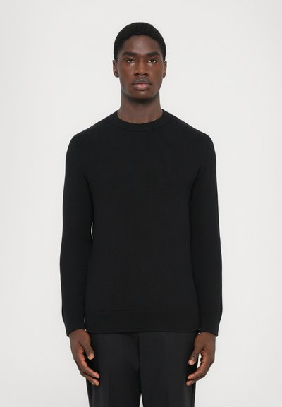 Maglione nero a costine con maniche lunghe e scollatura rotonda. Il tessuto ha una finitura strutturata e una silhouette aderente.