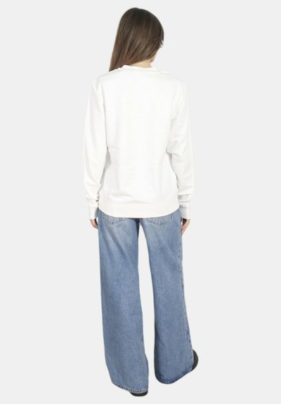 Felpa bianca con scollatura rotonda e maniche lunghe abbinata a jeans blu a gamba larga. Il tessuto sembra liscio con cuciture sottili.