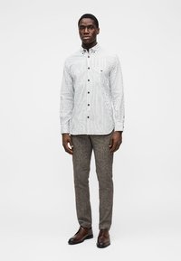 Camisola de manga comprida às riscas em branco e azul-marinho, com colarinho abotoado, combinada com calças cinzentas texturizadas e sapatos castanhos de atacadores.