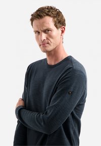 Donkerblauwe crewneck trui van gestructureerde stof, met ribgebreide manchetten en een klein logo op de linker mouw.