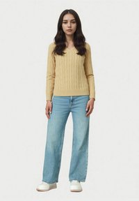 Pulover galben cu model torsadat și decolteu în V, asortat cu blugi largi, bleu deschis, și adidași albi. Estetică simplă și curată.