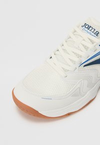 Chaussure de sport blanche avec une tige en mesh, accents bleus et semelle en caoutchouc. Elle dispose de lacets et d'un motif texturé sur le côté.