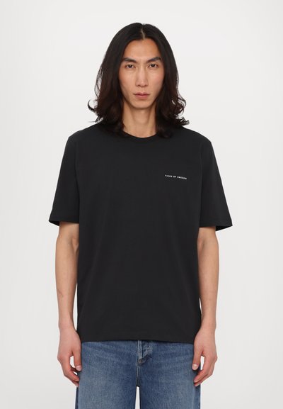 Tricou din bumbac negru, cu guler rotund, mâneci scurte și un mic logo alb pe piept. O pereche de blugi din denim bleu deschis.