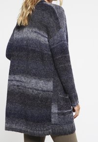 Gebreid vest in tinten van donkerblauw en grijs, met een losse pasvorm, lange mouwen en twee zijzakken, gemaakt van een zachte textuur.