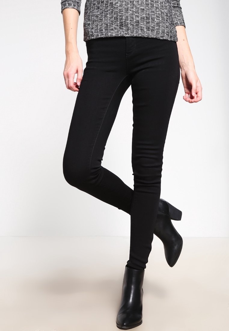 Jean skinny noir avec une texture lisse et un détail de couture subtil, associé à des bottines noires avec un talon épais.
