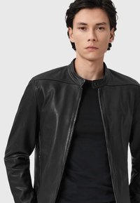 Zwarte leren jack met ritssluiting, staande kraag en gladde textuur. Draag het over een slim fit zwart shirt. Minimalistisch design.