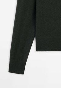 Pull en maille vert foncé avec une finition texturée, comprenant un poignet et un ourlet côtelés. Le tissu semble doux et extensible.