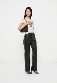 Camiseta beige con un gráfico negro en forma de triángulo, combinada con pantalones de cuero sintético negro de tiro alto; modelo sosteniendo un bolso negro.