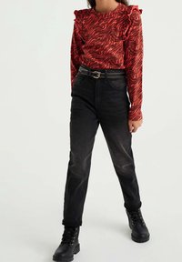 Röd långärmad topp med vågmönster och volangärmar, kombinerad med svarta jeans med hög midja och svarta snörskor.