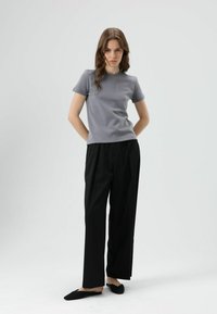 Grijs T-shirt met korte mouwen en een ronde hals, gecombineerd met zwarte, hooggetailleerde, geplooide broek. Outfit compleet gemaakt met zwarte instapschoenen.