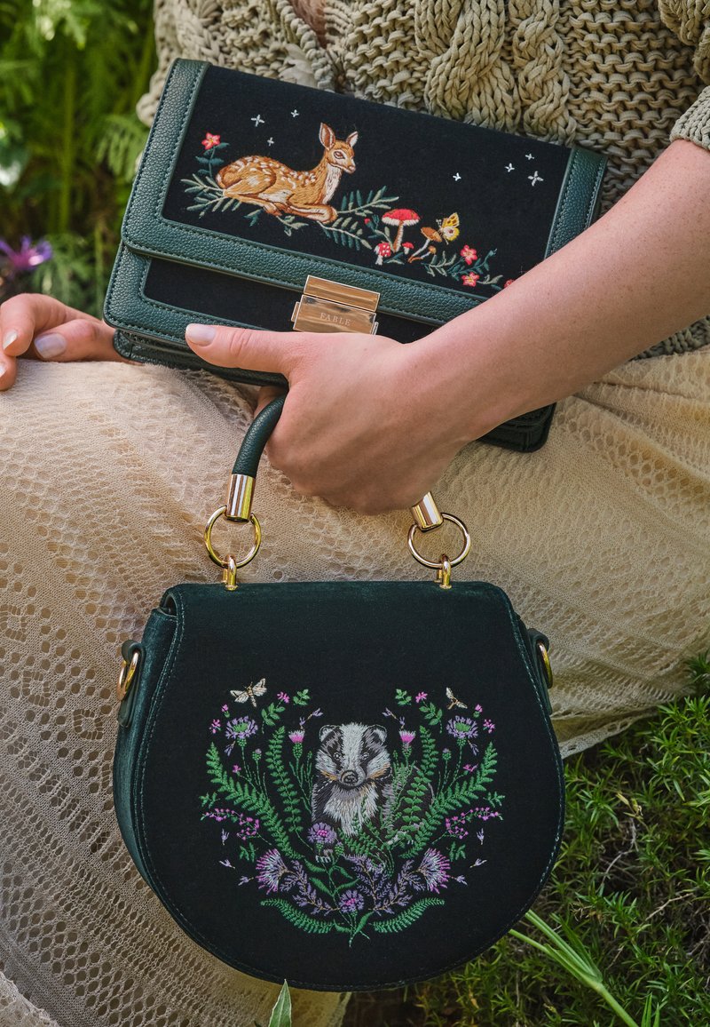 Gröna broderade väskor i veganskt läder, en med ett mönster av en hjort och blommor, den andra med en grävling, med guldfärgade detaljer och texturerade inslag.