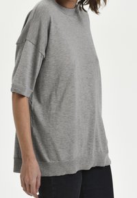 Lys grå strikket bluse med rund hals, drop-skulder og ribbede kanter. Stoffet ser blødt og let tekstureret ud.